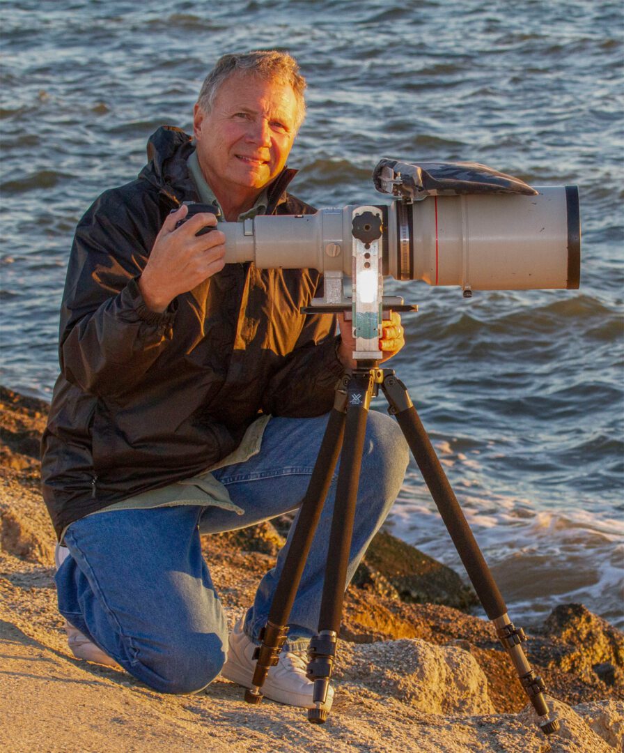 A man kneeling down to take a picture of the ocean.